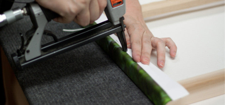 A photo showing a canvas print being stretched and stapled onto a frame.  All canvas pieces are finished by hand using high quality stainless steel upholstery staples. 